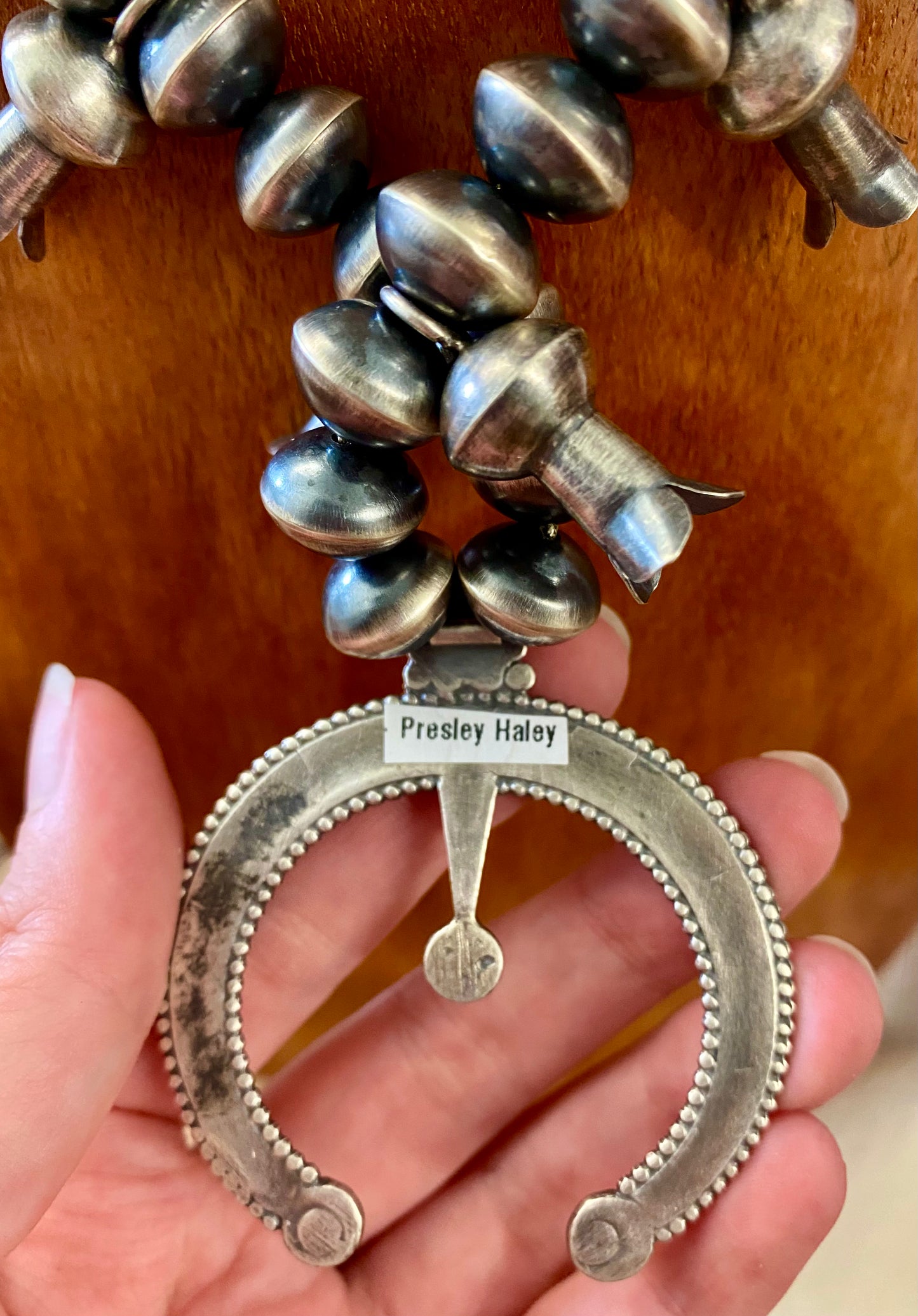 This sterling silver Silver Squash Blossom Necklace has a vintage feel. At the center, the Naja is 2-1/4" tall and 2-1/8" wide and is accented with 10 total flared blossoms 5 going up each side which are 1" inch long. These are strung on smooth, 12 mm Desert - Navajo Pearl strand. This necklace was given an old pawn satin buffing, and handcrafted by Native American artist and silversmith Presley Haley.
