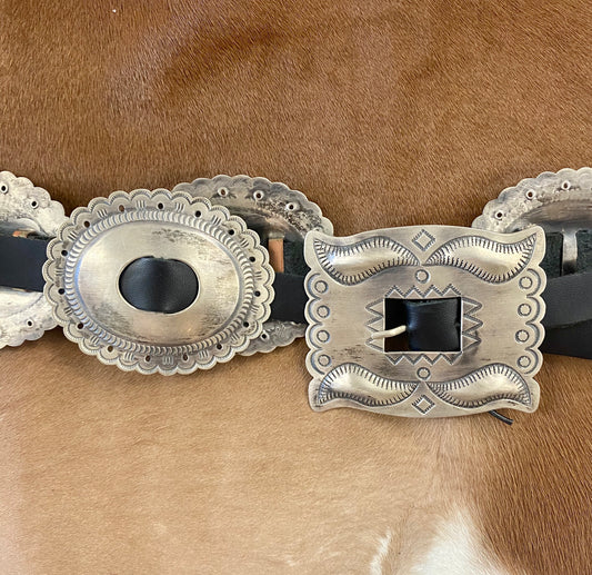 The Sterling Concho Belt - Ny Texas Style Boutique 44” inches from buckle to end of black leather silver Native American made Concho sterling silver signed large concho belt. Signed "RS" on the back of the buckle piece by native artist silversmith Roger Skeet. This beautiful handmade concho belt features 8 Conchos plus buckle piece. The perfect silver concho belt on black leather to add to your accessory wardrobe. Hallmark/Artist: Roger Skeet, Navajo