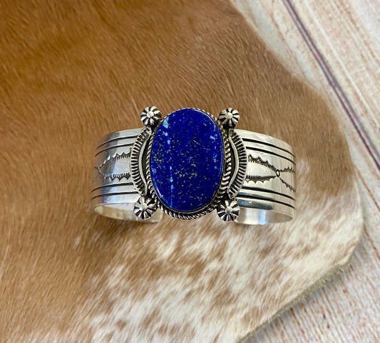 An absolutely stunning large single blue lapis stone with stamped silver detailing down the sides sterling silver cuff bracelet. This is a amazing statement piece that you are sure to receive compliments on! A piece that can be cherished and passed down generations for your children and grandchildren to admire for decades as well as lifetimes to come. Made by the talented Native American artist and silversmith Irene Kee. This beauty is stamped STERLING and signed "I. KEE" inside of the cuff bracelet.