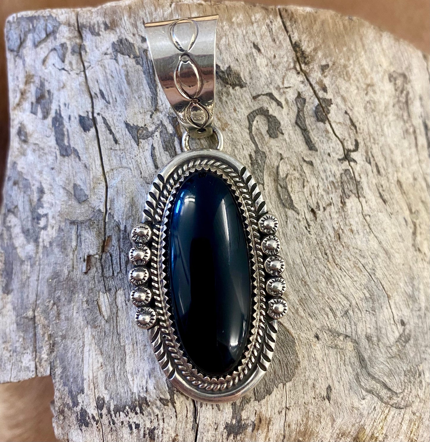The perfect single stone sterling silver Native American made onyx pendant to add to any necklace. This piece will look especially gorgeous on a strand of Navajo pearls. Stamped sterling and signed PY by Native artist silversmith Phillip Yazzie. Size: 2” inches length without bale x 1” inch width - 1” inch bale Signed: YES "PY" Hallmark/Artist: Phillip Yazzie Stone: Onyx