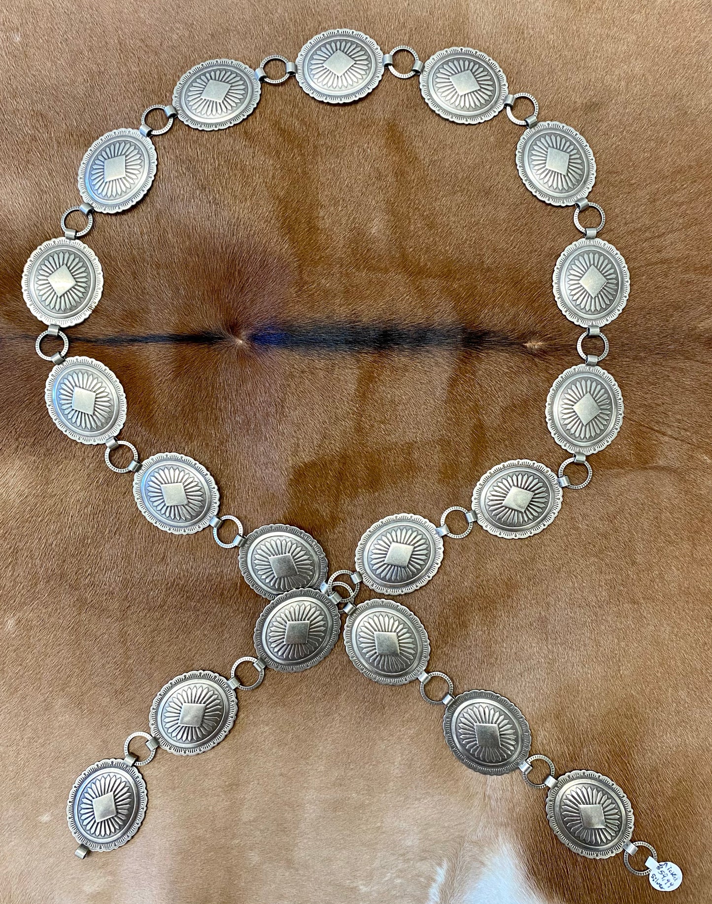 Beautiful 19 piece concho Nickle silver belt. This belt is adjustable as you can latch it on to any of the round pieces in-between the concho pieces. Each concho piece has a design etched on to it. This belt is amazing and will go so well with any outfit. Everyone needs a concho belt in their accessory wardrobe.   Size: 43” inches   1.25” x 1.5” inches Concho pieces 