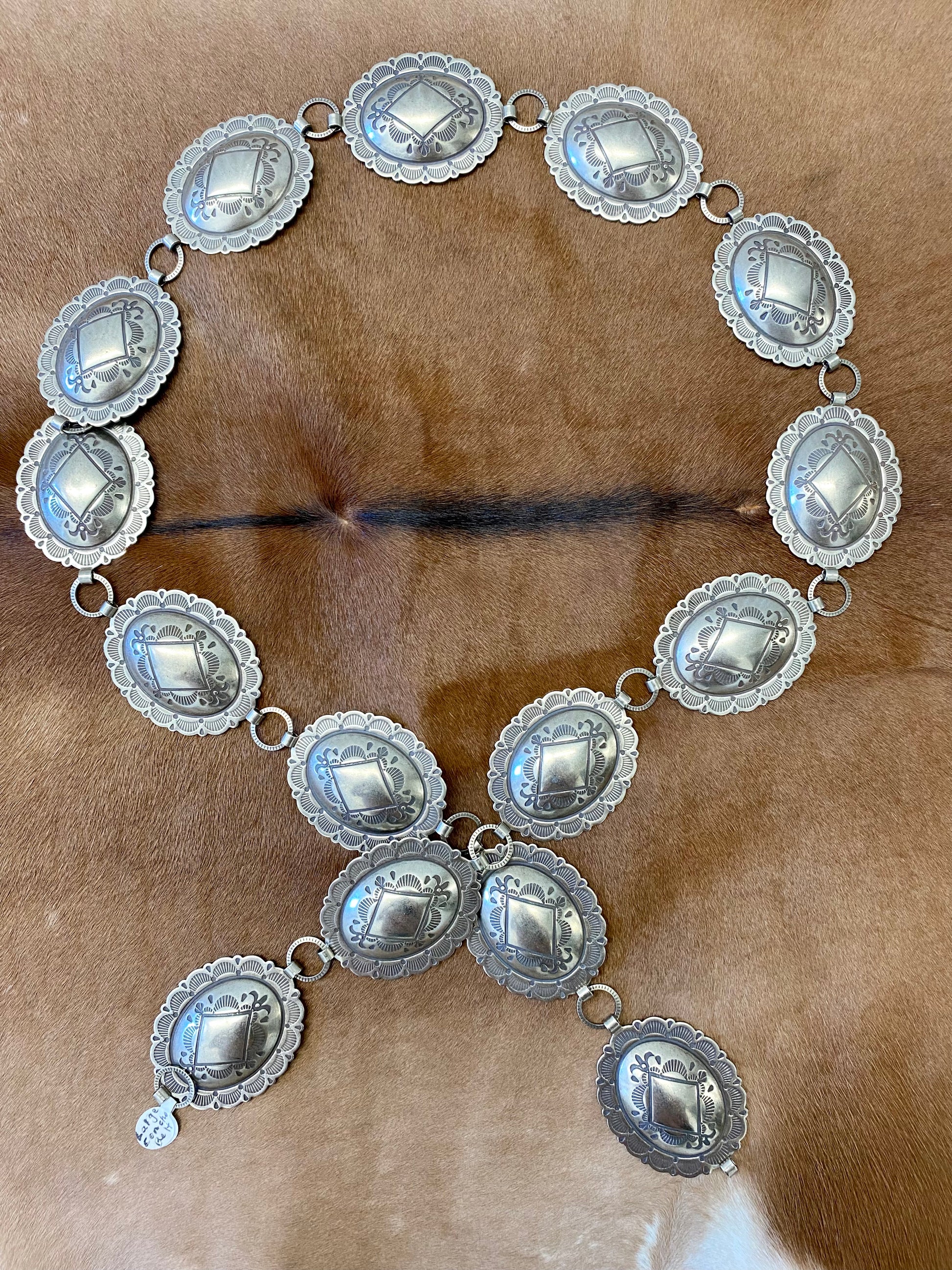 Beautiful 15 piece concho Nickle silver belt. This belt is adjustable as you can latch it on to any of the round pieces in-between the concho pieces. Each concho piece has a design etched on to it. This belt is amazing and will go so well with any outfit. Everyone needs a concho belt in their accessory wardrobe.   Size: 42” inches   15 Concho pieces each 1.75” x 2” inches 