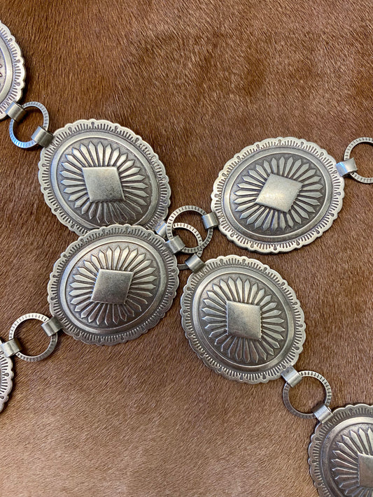 Beautiful 19 piece concho Nickle silver belt. This belt is adjustable as you can latch it on to any of the round pieces in-between the concho pieces. Each concho piece has a design etched on to it. This belt is amazing and will go so well with any outfit. Everyone needs a concho belt in their accessory wardrobe.   Size: 43” inches   1.25” x 1.5” inches Concho pieces 