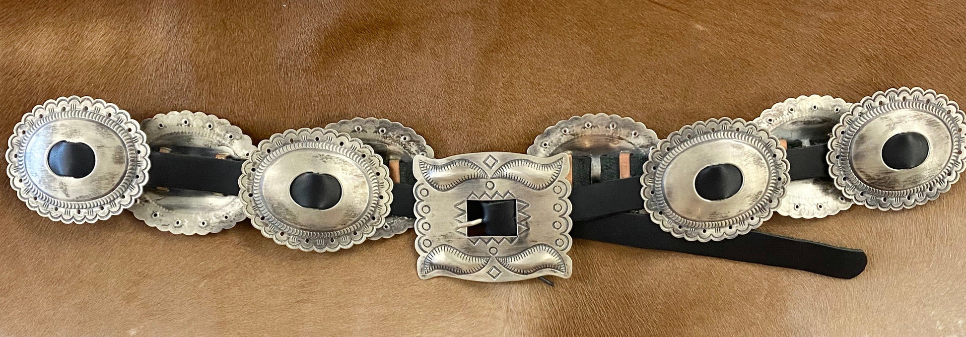 The Sterling Concho Belt - Ny Texas Style Boutique 44” inches from buckle to end of black leather silver Native American made Concho sterling silver signed large concho belt. Signed "RS" on the back of the buckle piece by native artist silversmith Roger Skeet. This beautiful handmade concho belt features 8 Conchos plus buckle piece. The perfect silver concho belt on black leather to add to your accessory wardrobe.   Hallmark/Artist: Roger Skeet, Navajo